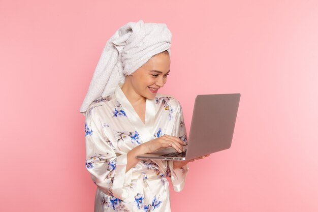 Eine junge schöne Dame der Vorderansicht im Bademantel, die mit Laptop arbeitet