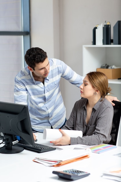 Eine junge schöne Dame der Vorderansicht im grauen Hemd, die etwas mit dem jungen Mann im Büro während der Tagesaufbaujobaktivität spricht und bespricht