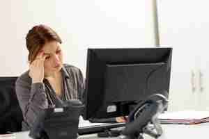 Kostenloses Foto eine junge schöne dame der vorderansicht im grauen hemd, die ihren pc verwendet, der in ihrem büro sitzt und denkt, während des tagesaufbaus jobaktivität zu berechnen