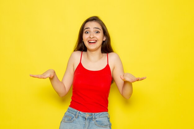 Eine junge schöne Dame der Vorderansicht im roten Hemd und in den blauen Jeans, die aufwerfen