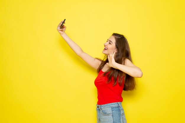 Eine junge schöne Dame der Vorderansicht im roten Hemd und in den blauen Jeans, die eine Selfie-Modellmädchenfarbfrau nehmen