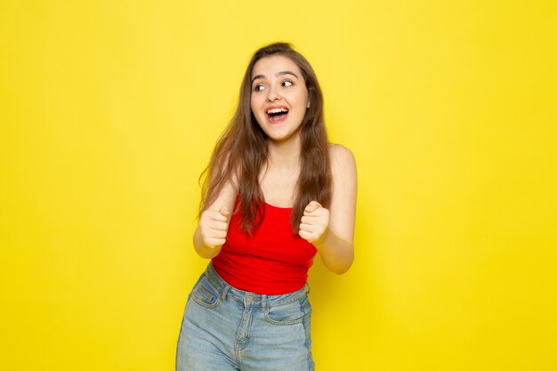 Eine junge schöne Dame der Vorderansicht im roten Hemd und in den blauen Jeans, die mit Freude aufwerfen