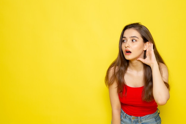 Eine junge schöne Dame der Vorderansicht im roten Hemd und in den blauen Jeans, die versuchen zu hören