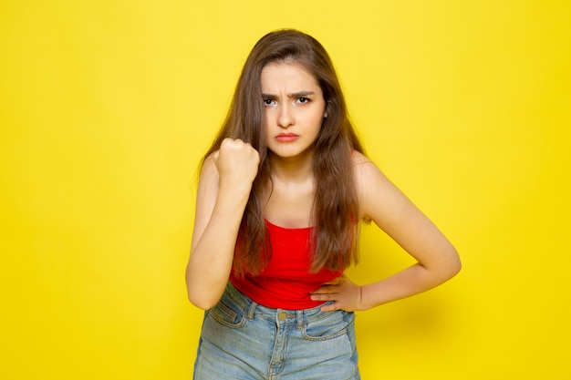 Eine junge schöne Dame der Vorderansicht im roten Hemd und in den blauen Jeans mit bedrohlichem Ausdruck