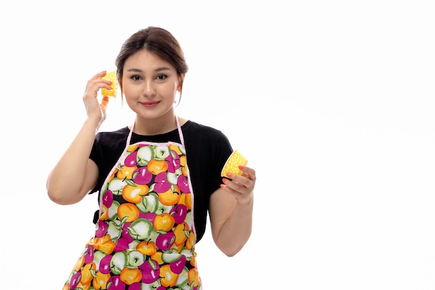 Eine junge schöne dame der vorderansicht im schwarzen hemd und im bunten umhang, die gelbe kleine kuchenformen lächelnd halten Kostenlose Fotos