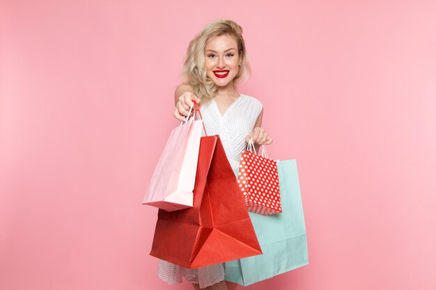 Eine junge schöne Dame der Vorderansicht im weißen Kleid, die Einkaufspakete mit Lächeln auf ihrem Gesicht hält