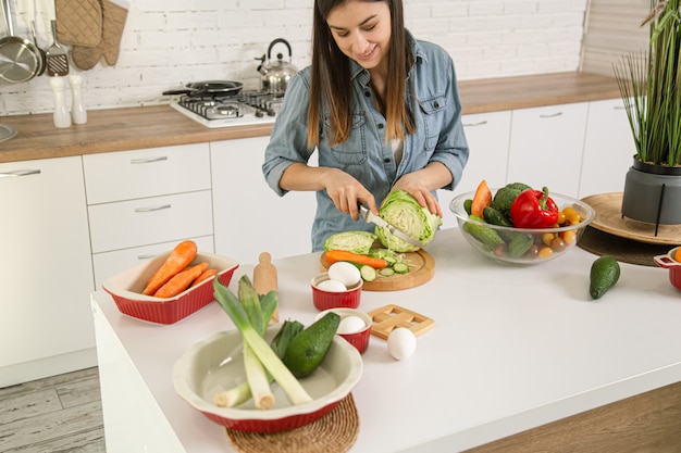 Eine junge schöne Frau bereitet in der Küche einen Salat mit verschiedenen Gemüsesorten zu.