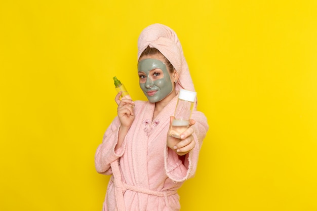 Eine junge schöne Frau der Vorderansicht im rosa Bademantel, der Flaschensprays mit Lächeln hält