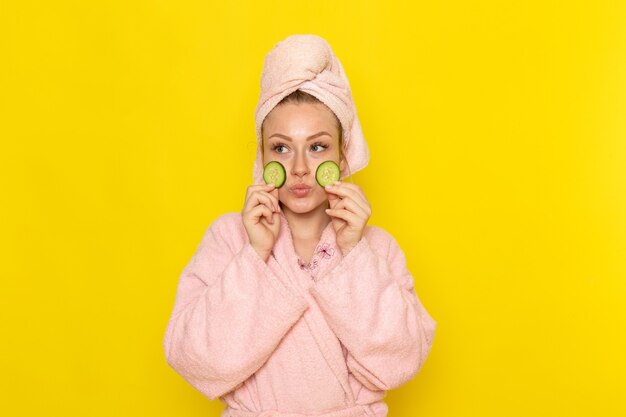 Eine junge schöne Frau der Vorderansicht im rosa Bademantel, der Gurkenscheiben hält