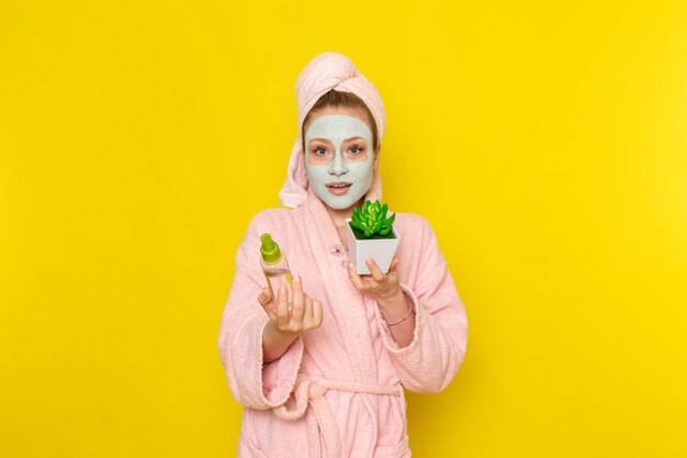 Eine junge schöne Frau der Vorderansicht im rosa Bademantel, der Spray und Pflanze hält