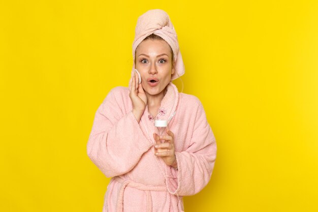 Eine junge schöne Frau der Vorderansicht im rosa Bademantel, die alles Make-up mit Reiniger aufräumt