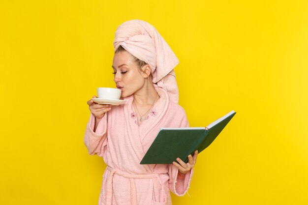 Eine junge schöne Frau der Vorderansicht im rosa Bademantel, die Tasse Tee und Heft hält