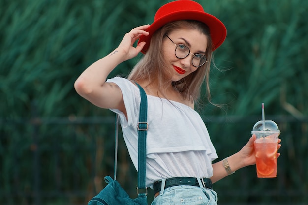 Eine junge stilvolle Frau, die ein erfrischendes Getränk beim Gehen hat