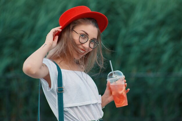 Eine junge stilvolle Frau, die ein erfrischendes Getränk beim Gehen hat