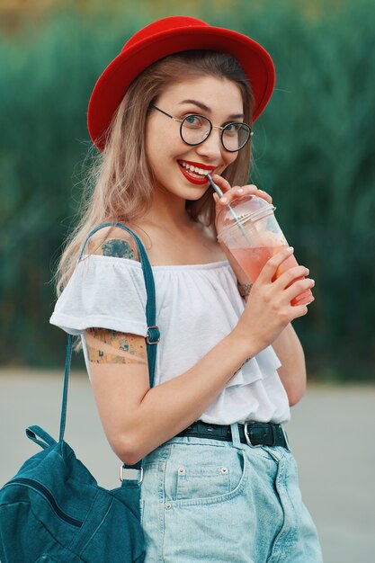 Eine junge stilvolle Frau, die ein erfrischendes Getränk beim Gehen hat