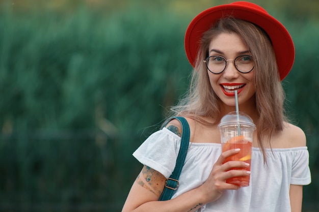 Eine junge stilvolle Frau, die ein erfrischendes Getränk beim Gehen hat