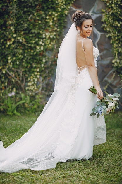 Eine junge und schöne Braut steht in einem Sommer Park mit Blumenstrauß