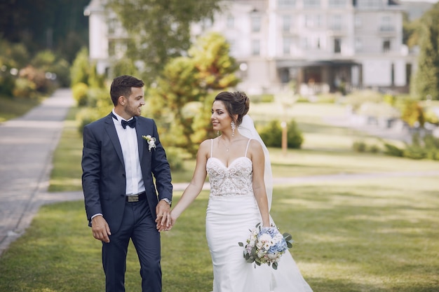 Eine junge und schöne Braut und ihr Ehemann, die in einem Sommerpark mit Blumenstrauß stehen