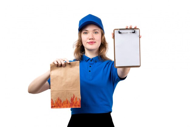 Eine junge weibliche Kurierarbeiterin der Vorderansicht des Lebensmittel-Lieferservices, die Lebensmittelpaket und Notizblock hält, die auf Weiß lächeln