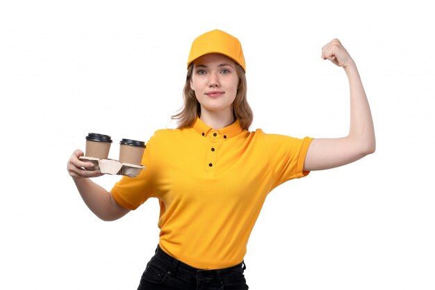 Eine junge weibliche Kurierfrau der Vorderansicht des Lebensmittellieferdienstes lächelnd, der Kaffeetassen hält und auf Weiß biegt