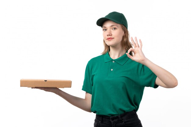 Eine junge weibliche Kurierin der Vorderansicht in der grünen Uniform, die Pizza-Lieferbox hält, die in Ordnung Zeichen zeigt