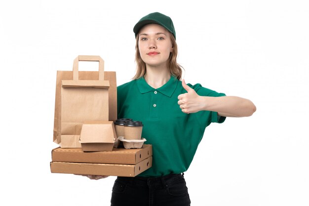 Eine junge weibliche Kurierin der Vorderansicht in der grünen Uniform lächelnd, die Kaffeetassen-Lebensmittelverpackungen hält, die wie Zeichen zeigen