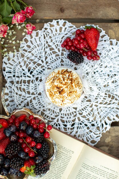 Eine Kaffee-Leckerei von oben Nahaufnahme zusammen mit verschiedenfarbigen Beeren auf dem weißen Taschentuch und der braunen Holzoberfläche