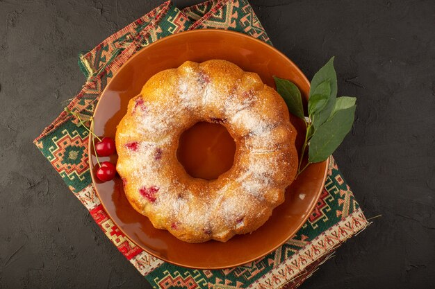 Eine Kirschkuchenrunde der Draufsicht, die innerhalb der braunen Platte gebildet wird, lecker auf dem dunklen Schreibtischkuchen-Kekszuckersüß