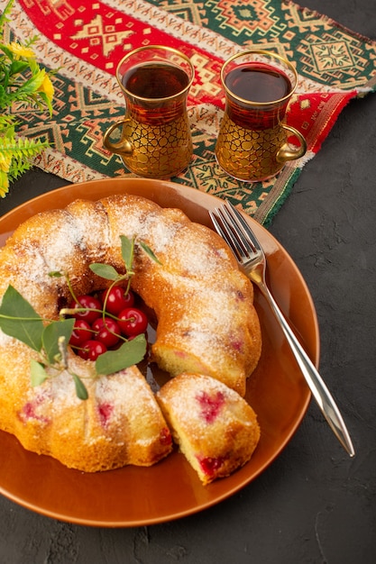 Kostenloses Foto eine kirschkuchenrunde der draufsicht gebildet innerhalb der braunen platte mit tee auf dem dunklen schreibtischkuchenkekszuckersüß