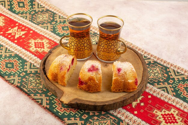 Eine Kirschkuchenscheibe von vorne sieht köstlich mit Tee auf dem braunen Holzschreibtisch und dem rosa Schreibtisch