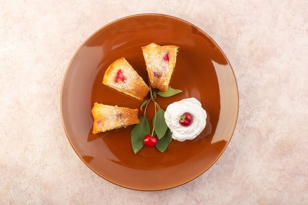 Eine Kirschkuchenscheiben der Draufsicht innerhalb der braunen Platte mit Kirschen auf dem rosa Schreibtischkuchen-Kekszuckersüß