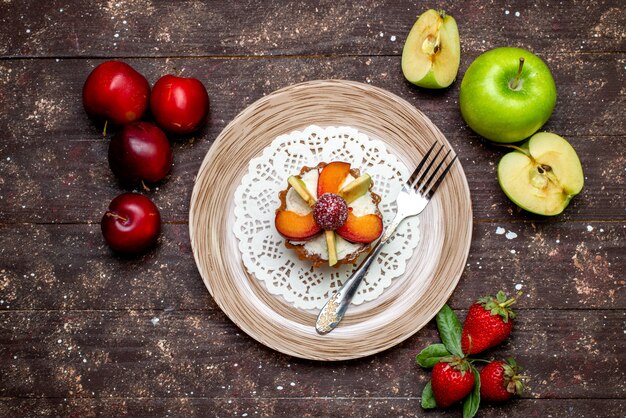 Eine kleine köstliche Torte der Draufsicht mit Sahne-Innenplatte mit frischen Erdbeeren und Äpfeln auf dem Kekskuchen des dunklen Hintergrundplätzchens