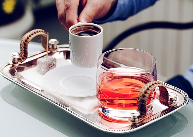 Eine kleine weiße Espressotasse mit einem Glas rotem Getränk.