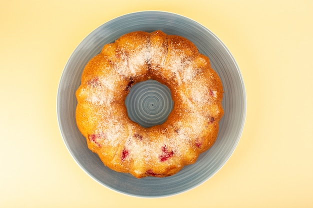 Eine köstliche Runde gebackener Obstkuchen der Draufsicht mit roten Kirschen innen und Zuckerpulver innen runder blauer Platte auf Gelb