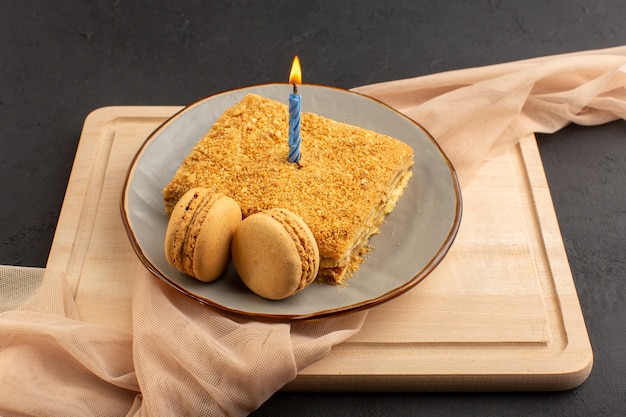 Eine Kuchenansicht der Vorderansicht lecker und Innenplatte mit Kerze gebacken. Macarons auf dem Holzschreibtisch und dunkler Kuchenkekszucker süß