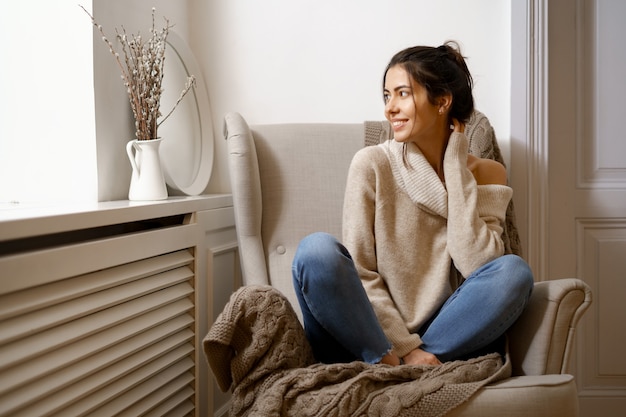 Eine lächelnde Dame in schicker trendiger Kleidung sitzt auf einem Sessel. Lächelnd, in entspannter Atmosphäre drinnen sitzen