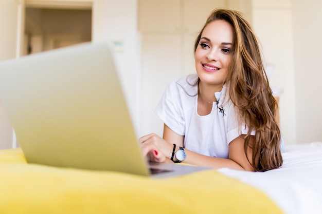 Eine lächelnde Frau, die mit leicht angehobenen Beinen zu Hause vor ihrem Laptop im Bett liegt