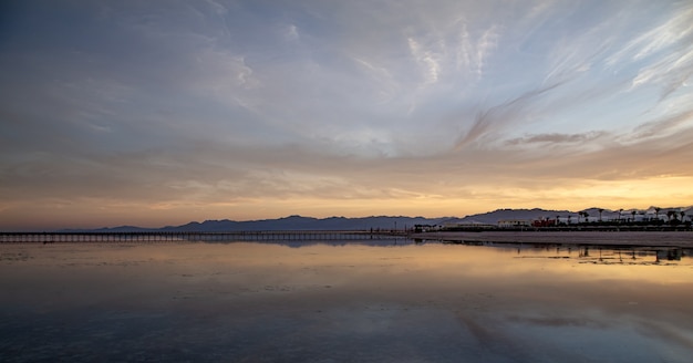 Eine Landschaft des Meeres mit einem langen Pier und Bergen am Horizont.