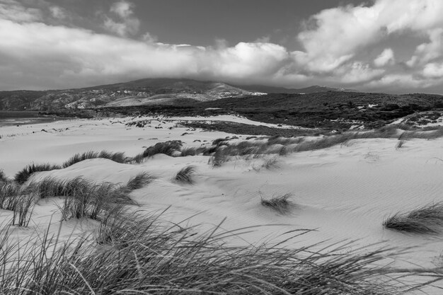 Eine Landschaft mit Gras bedeckt mit Sand, umgeben von Bergen unter den Gewitterwolken