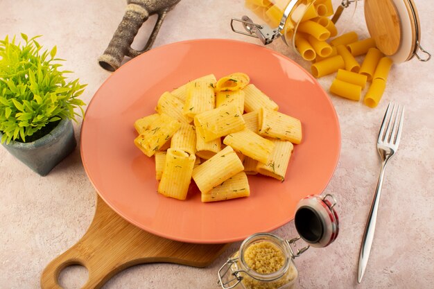 Eine leckere Mahlzeit der italienischen Pasta der Draufsicht innerhalb des rosa Tellers zusammen mit Blume und rohen Nudeln auf rosa