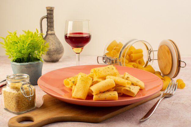 Eine leckere Mahlzeit der italienischen Pasta der Vorderansicht innerhalb des rosa Tellers zusammen mit Blume und rohen Nudeln auf rosa