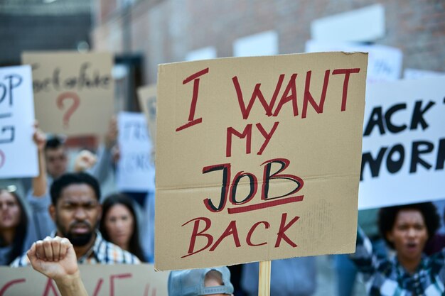 Eine Menge Arbeitsloser, die gegen den Verlust ihres Arbeitsplatzes aufgrund einer Coronavirus-Pandemie protestieren Konzentrieren Sie sich auf das Banner mit der Aufschrift „Ich möchte meinen Job zurück“.