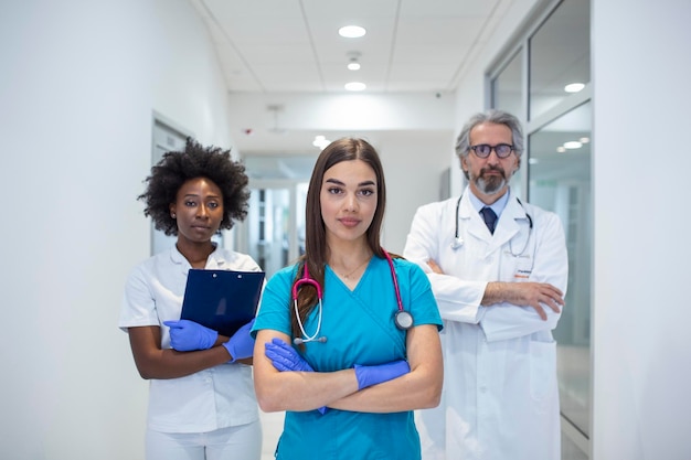 Eine multiethnische Gruppe von drei Ärzten und Krankenschwestern, die in Kitteln und Kitteln auf einem Krankenhauskorridor stehen. Das Team von Mitarbeitern des Gesundheitswesens starrt in die Kamera und lächelt