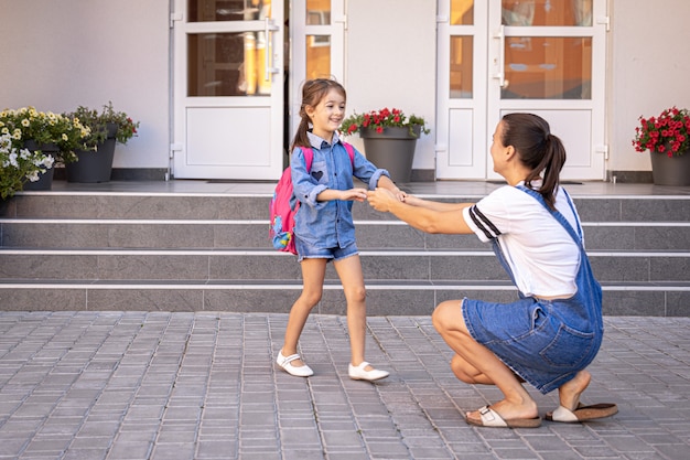 Eine Mutter begleitet den Schüler zur Schule, ein glückliches kleines Mädchen mit einer fürsorglichen Mutter, zurück zur Schule.