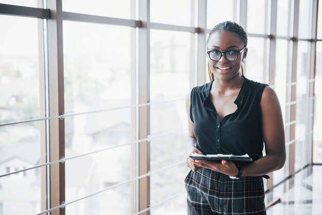 Eine nachdenkliche afroamerikanische Geschäftsfrau, die Brillen hält, die Dokumente halten