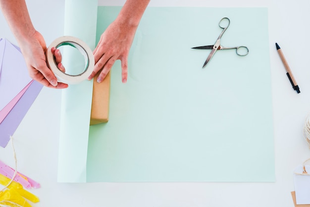 Kostenloses Foto eine obenliegende ansicht der hand der frau das papier auf geschenkbox über dem weißen schreibtisch haftend