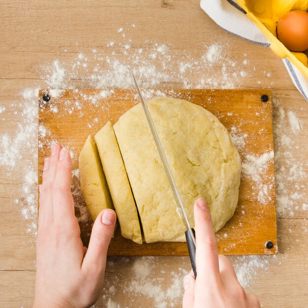 Eine obenliegende Ansicht der Hand der Frau den Teig für das Zubereiten der italienischen Gnocchiteigwaren auf Holztisch schneiden