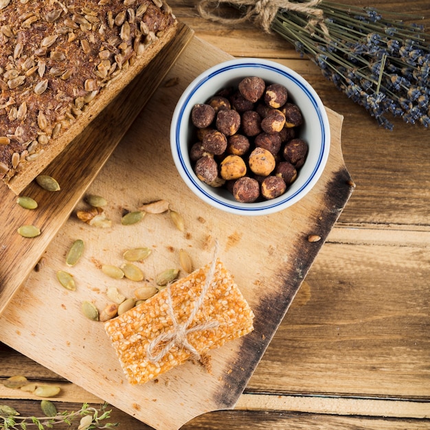 Eine obenliegende Ansicht der Haselnussschüssel mit Brot und Stange des indischen Sesams auf hackendem Brett