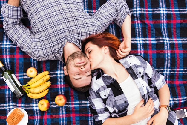 Eine obenliegende Ansicht der jungen Frau ihren Freund küssend, der auf Decke liegt