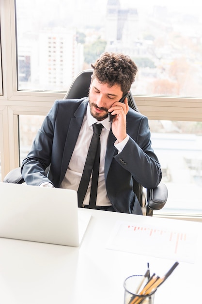 Eine obenliegende Ansicht des jungen Geschäftsmannes sprechend am Handy am Arbeitsplatz